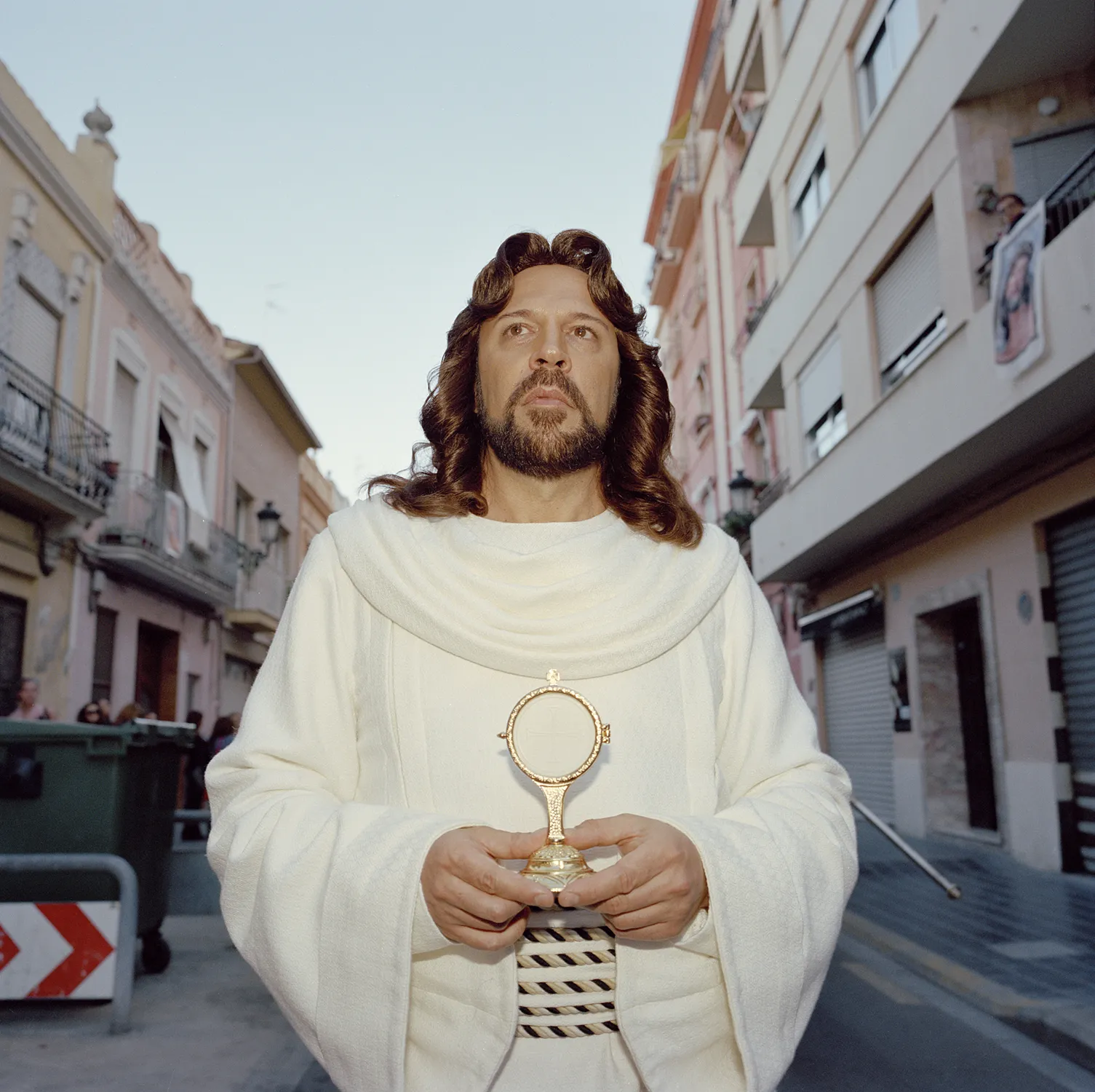 Hombre caracterizado de Jesucristo sosteniendo un relicario dorado en medio de una calle, parte del proyecto Quisiera que siempre fuera así de Laura Silleras.