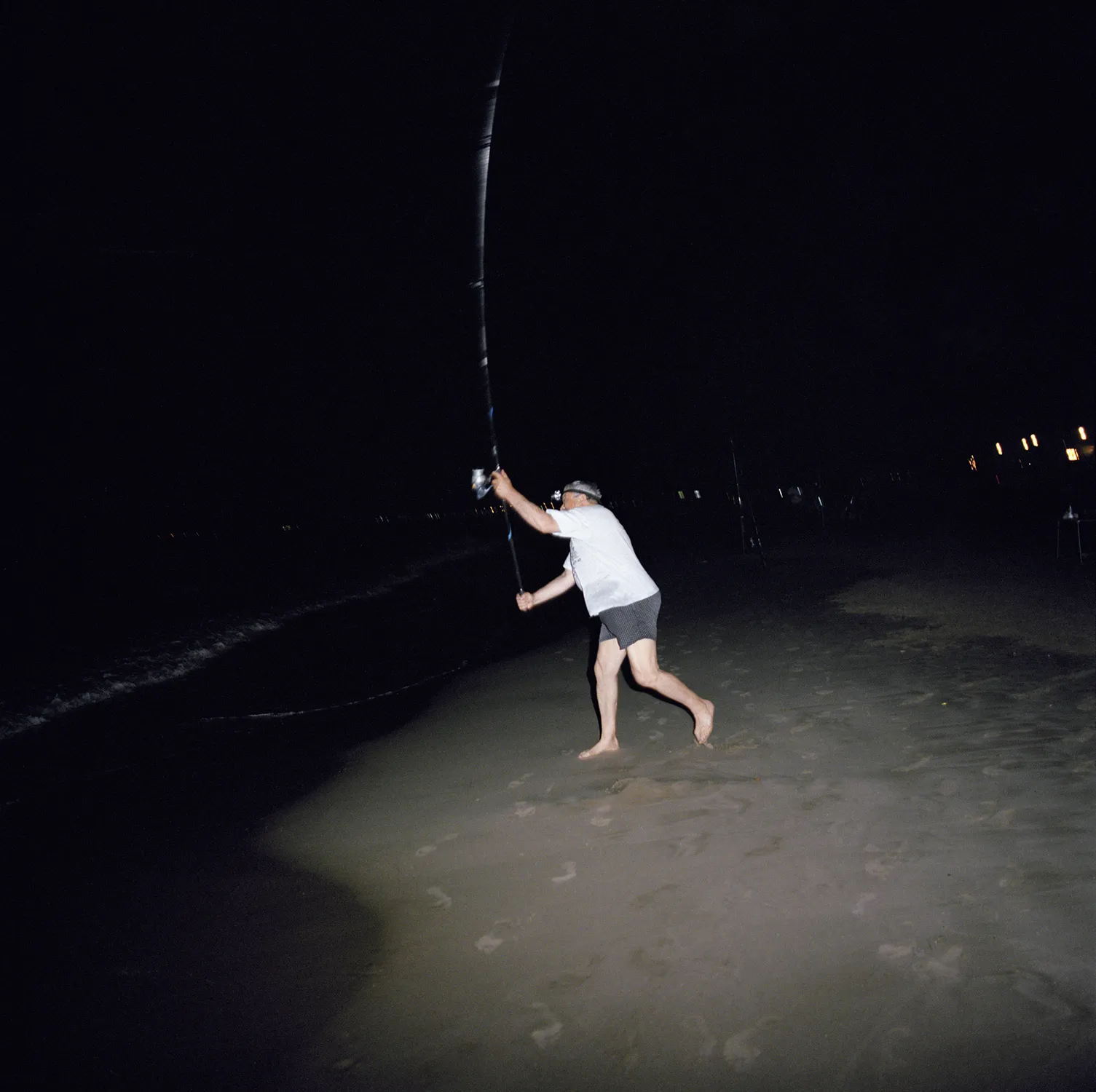 Pescador lanzando su caña de noche en la orilla de la playa bajo la luz de un flash, obra del proyecto Quisiera que siempre fuera así de Laura Silleras.