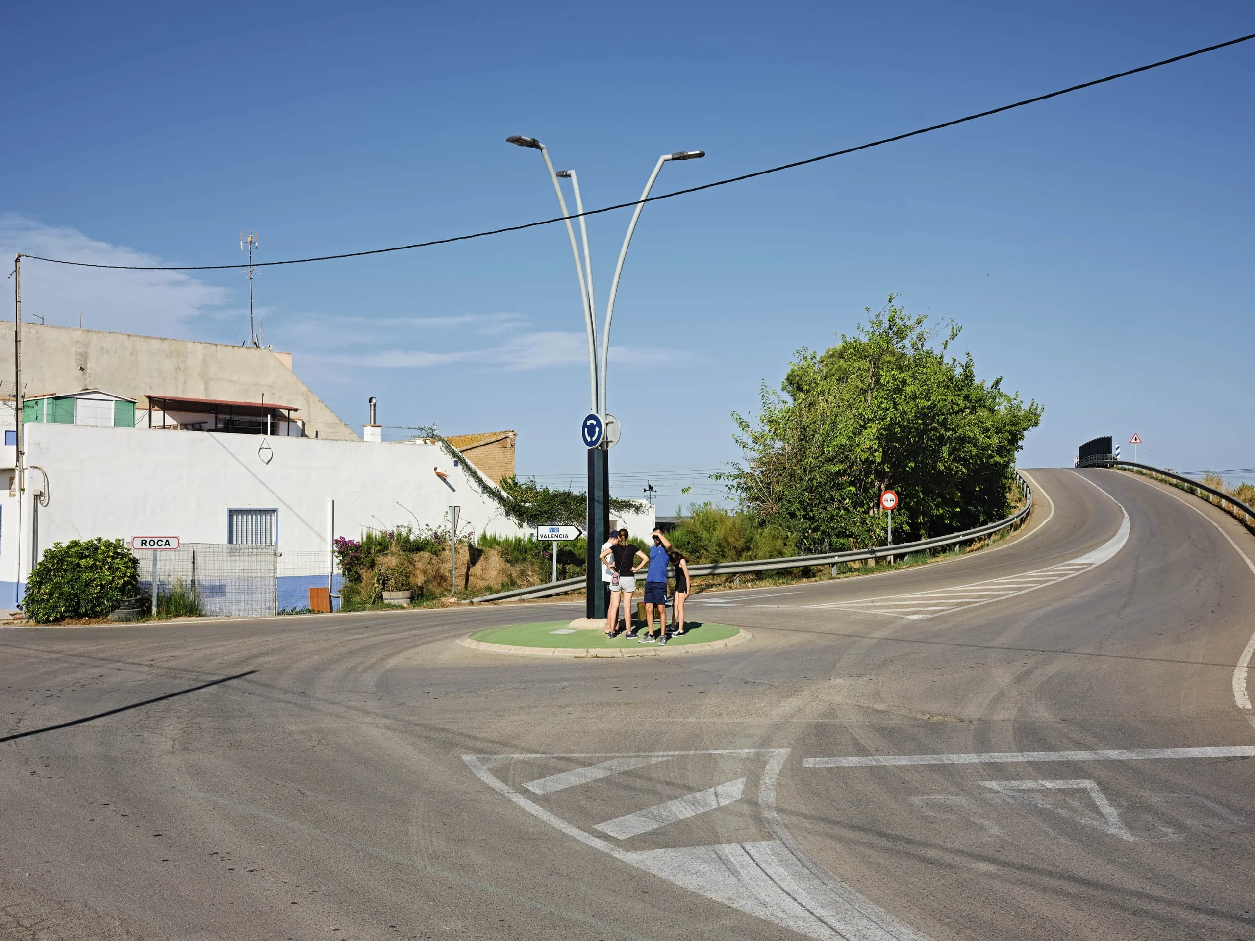 Grupo de personas paradas en la isleta central de una rotonda bajo una farola de gran altura, perteneciente al proyecto La idea de éxito de Markel Redondo.